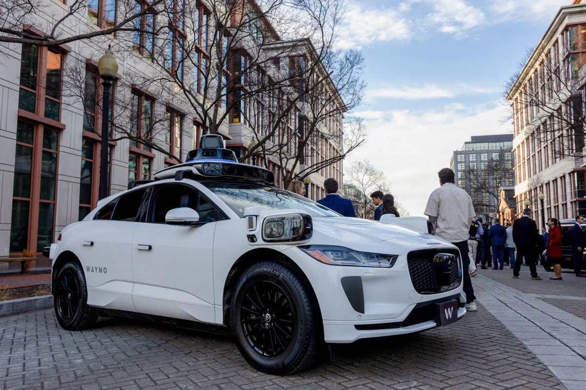 A single driverless car calmly parked in the middle of a coned-off construction zone with a loading bar over it.