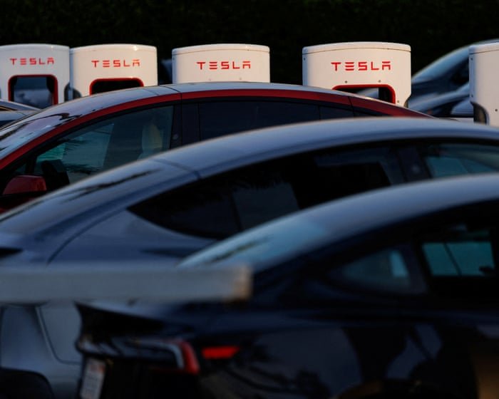 A single red Tesla driving off a ramp toward a floating robot in the clouds, held up by a rope tied to a stack of car keys.