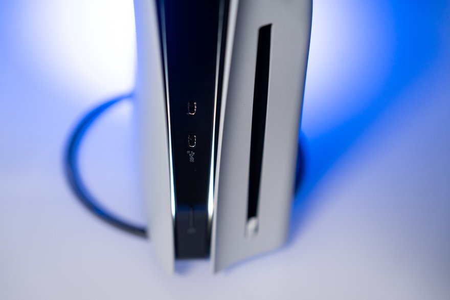 A single PlayStation game disc lying in an open coffin with a lily on top, gleaming under a spotlight.