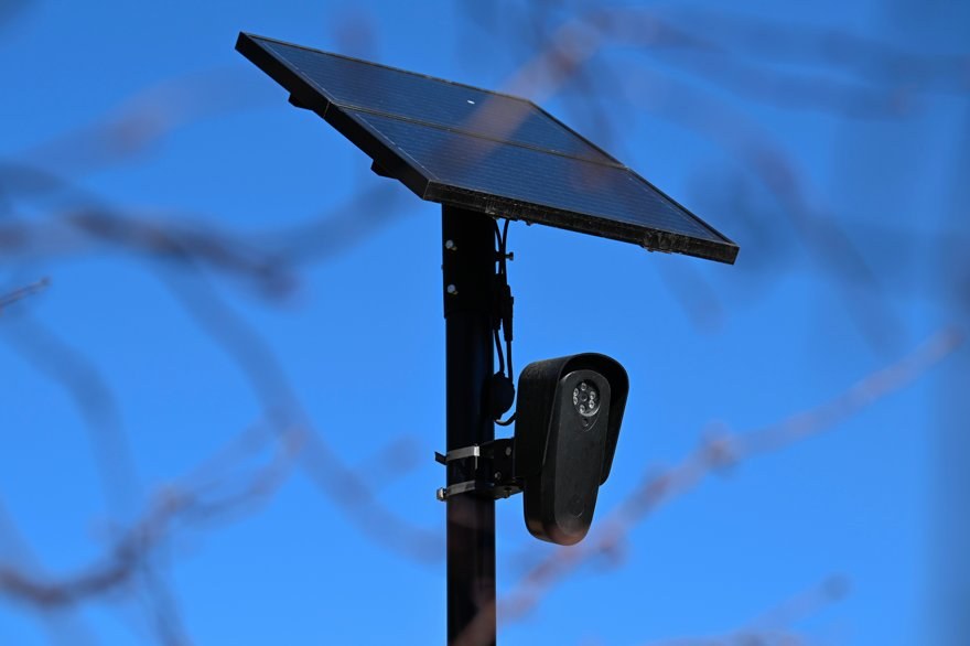 A lone sticky note with a scribbled password stuck to a giant surveillance camera on a pole.